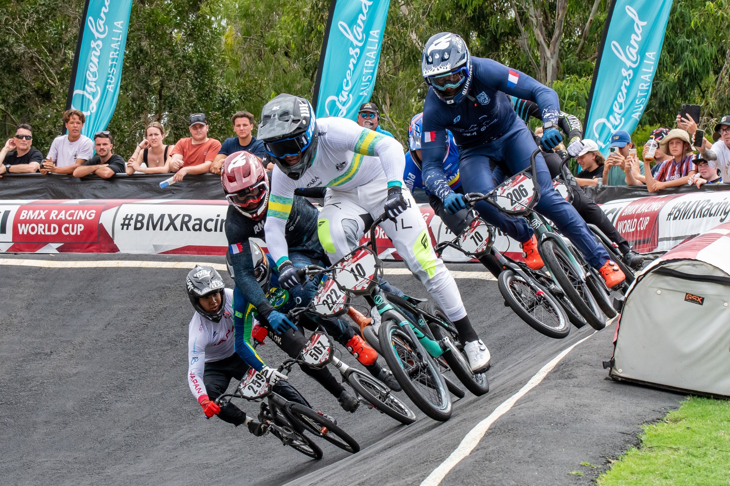 BMX Racing athletes negotiate a bend as the crowd watches on at the Brisbane SX International BMX Centre during a UCI BMX Racing World Cup in 2024.